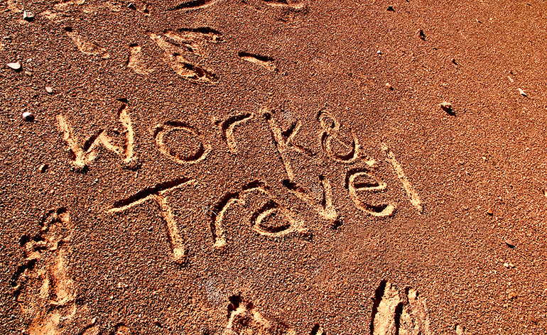 The words work and travel sketched on a beach in Australia.