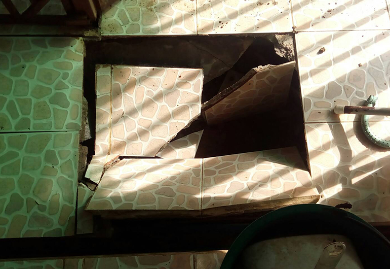 Broken floor tiles and a hole in the ground.