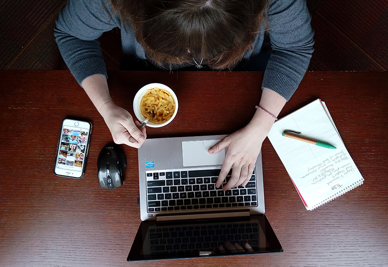 A table with a laptop, mac and cheese, list and smartphone to depict the difficulty in finding a balance.