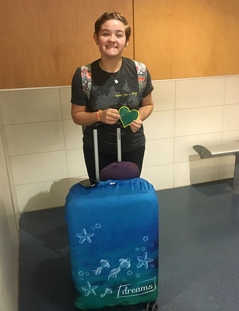 Greenheart Traveler, Emmy Scott, with her luggage and a green heart sticker.
