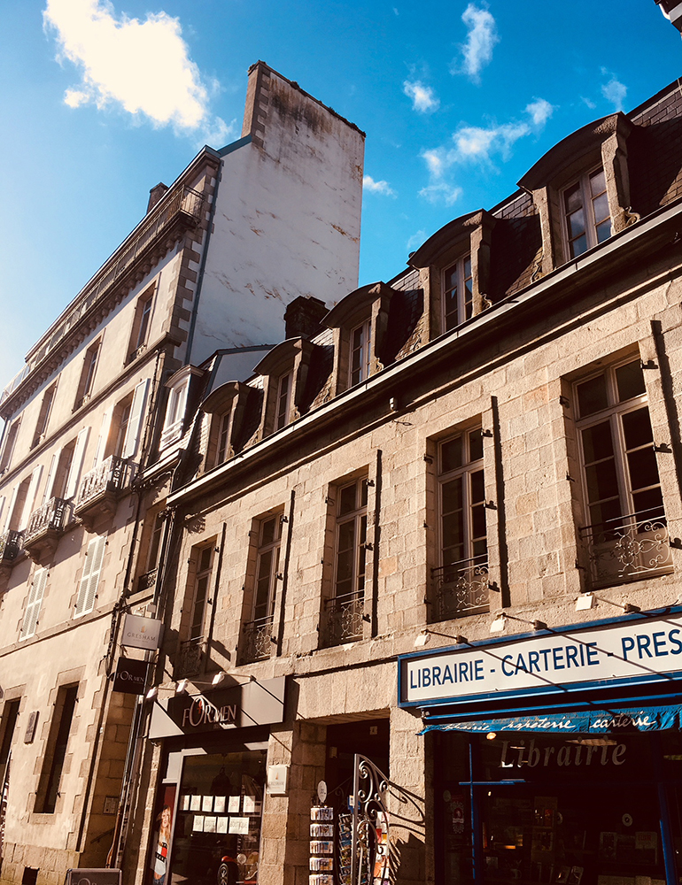 French architecture of buildings on a street and a book and paper shop.