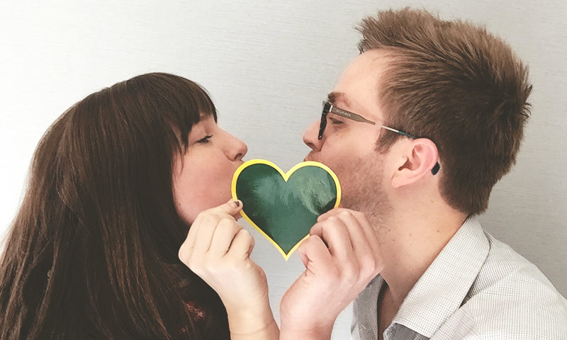 Kissing behind a Greenheart Travel sticker.
