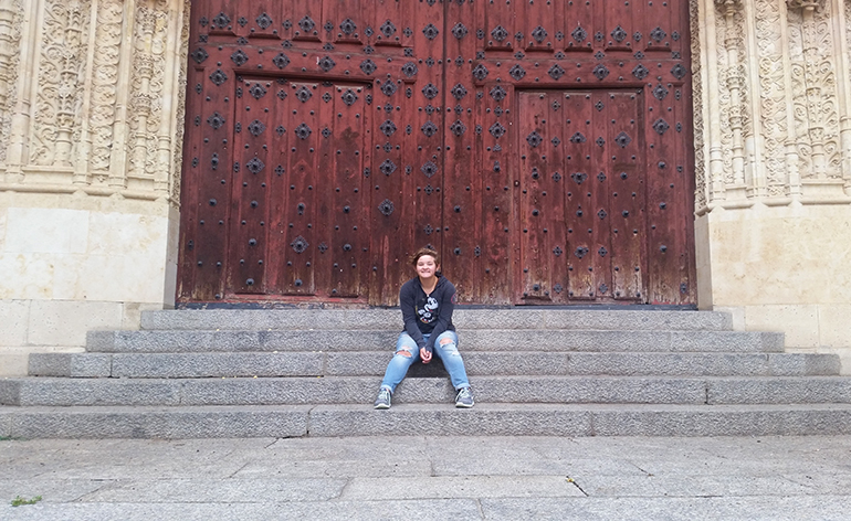 Greenheart Traveler, Emmy Scott, sitting in front of doors in Spain.
