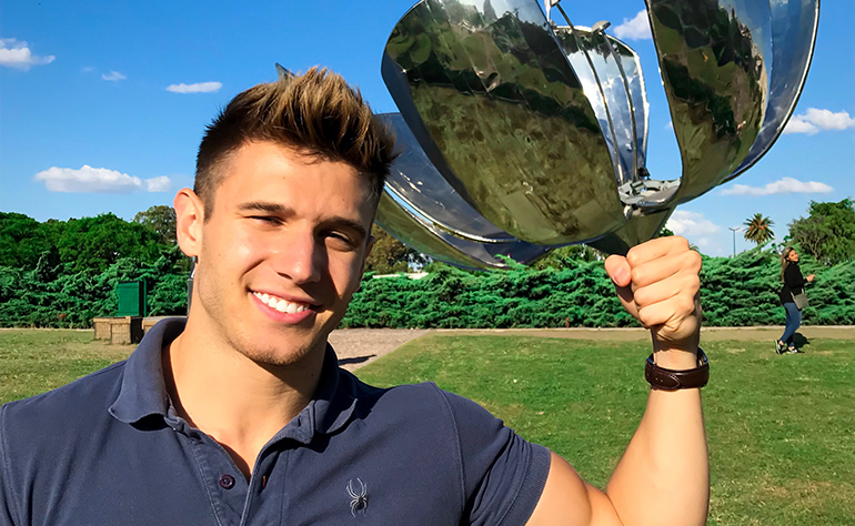 Greenheart Traveler, Sam Cushing, posing with a metal sculpture.