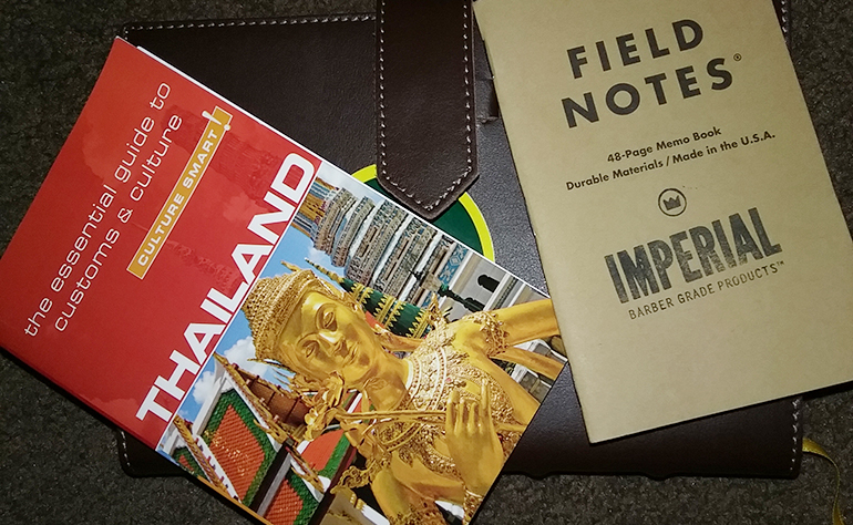 A Thailand guidebook, a Greenheart Travel sticker and a notebook.