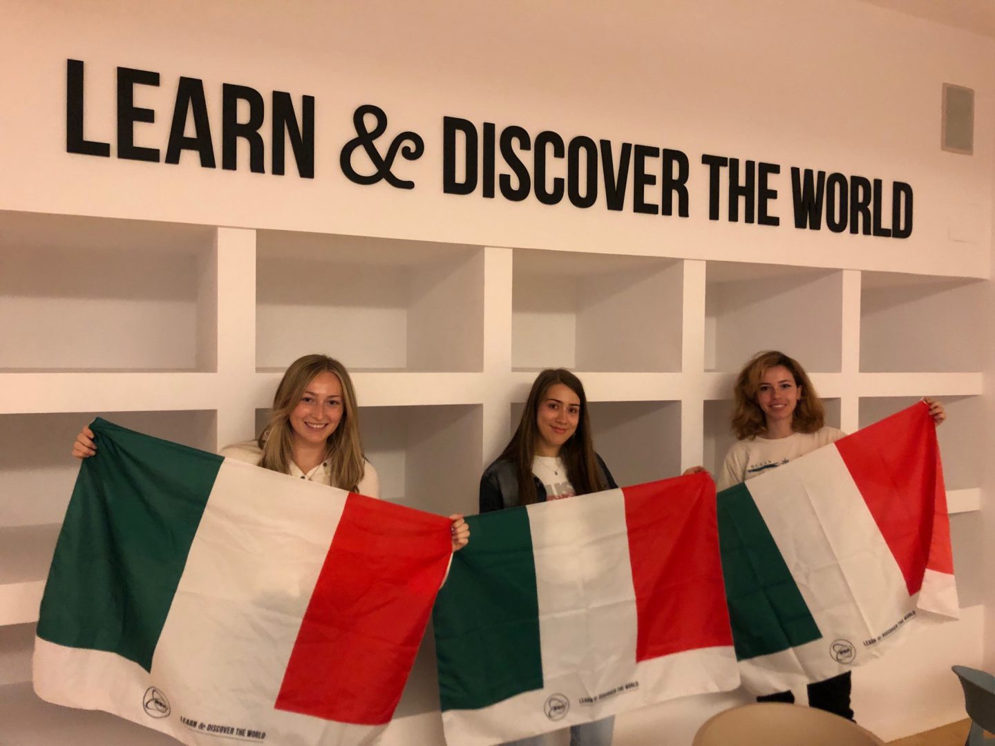 three women each hold an Italian flag underneath a sign that says 